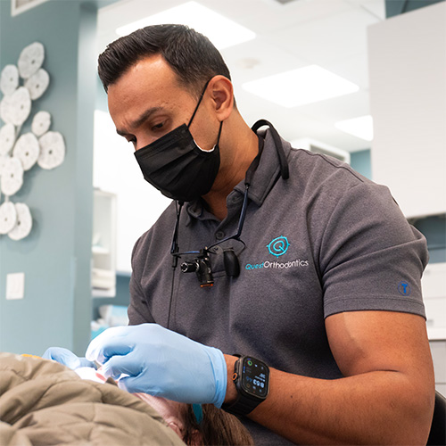dr patel working on a patient in dental chair, while wearing gloves and a face mask